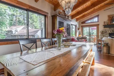 a large wooden table in a living room with windows at Boathouse in the Woods by Tahoe Getaways - Minutes to Lake Tahoe & Northstar in Kings Beach