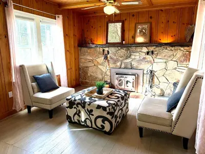 a living room with two chairs and a stone fireplace at Cozy Farm House with River access in Three Rivers