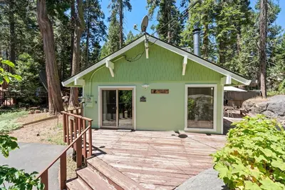 a green house with a porch and a wooden deck at Happy Bear- Family & Pet Friendly in Shaver Lake