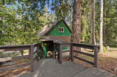 a green cabin in the woods with a wooden bridge at Blue Meadow-Family Pet Friendly & near the lake in Shaver Lake