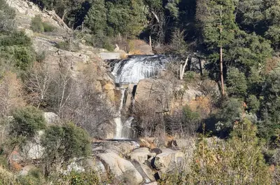 a waterfall on the side of a mountain with trees at Skyfalls Retreat Mid-Century Guesthouse near Yosemite in Oakhurst
