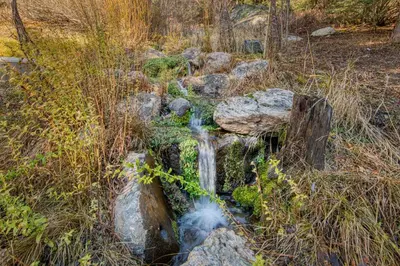 a small waterfall in a field with rocks and grass at Painted River Retreat by Tahoe Getaways - 4BR w River Views, Hot Tub & EV Charger. in Truckee