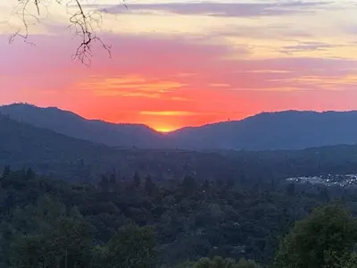 a sunset over a forest with mountains in the background at Sunset Cottage near Yosemite in Oakhurst