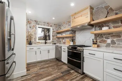 a kitchen with white cabinets and a stone wall at Dogwood Retreat- Family friendly Epic Views in Shaver Lake