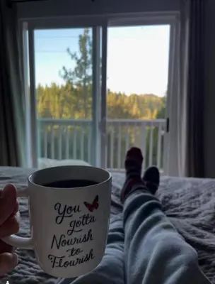 a person is holding a coffee cup on a bed at StayCation Sierra – Nonpareil Retreat in Groveland