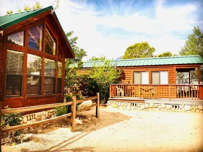 a log cabin with a porch and a green roof at Boulder Creek RV Resort in Lone Pine