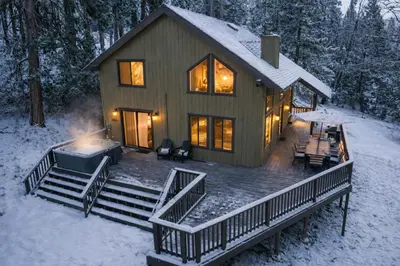 a house with a deck in the snow at Shaver Escape Hot Tub Cabin Retreat with AC in Shaver Lake