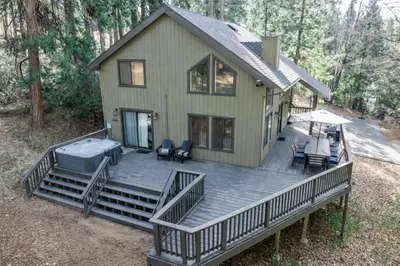 a house with a large deck in the woods at Shaver Escape Hot Tub Cabin Retreat with AC in Shaver Lake