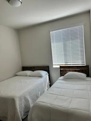 two beds in a room with a window with white sheets at Prime Location Residence in Manteca