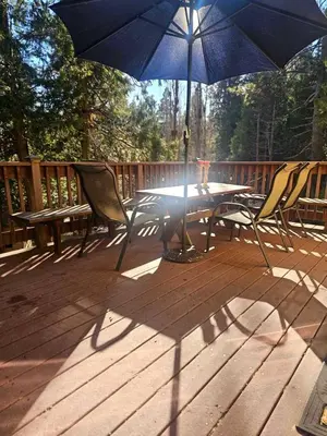 a table and chairs with a blue umbrella on a deck at Peaceful Mountain Cabin with Private Lake and Game Room Near Long Barn, California in Long Barn