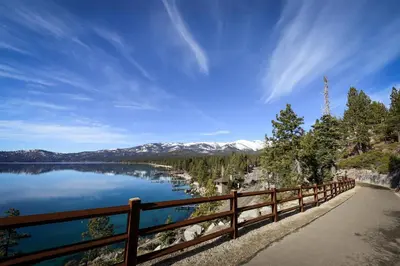 a wooden fence next to a lake with snow covered mountains at Incline Village Creekside Retreat in Incline Village
