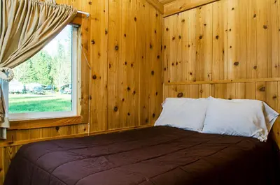 a bedroom with wooden walls and a bed with a window at Yosemite Lakes Cabin & Cottages in Harden Flat