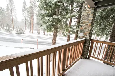 a snow covered porch with a wooden railing and trees at Summit 211 Apartment in Mammoth Lakes