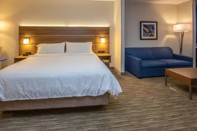 a hotel room with a bed and a blue couch at Holiday Inn Express Hotel & Suites Roseville - Galleria Area by IHG in Roseville