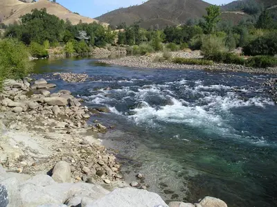 a river with some rocks and water and mountains at Ponderosa Camping Resort One-Bedroom Cabin 2 in Lotus