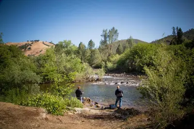 two men and a dog standing in a river at Ponderosa Camping Resort One-Bedroom Cabin 4 in Lotus