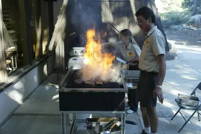two people cooking food on a grill with flames at Snowflower Camping Resort Cabin 3 in Emigrant Gap