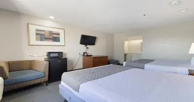 a hotel room with two beds and a chair and a television at Budget Inn and Suites Stockton Yosemite in Stockton