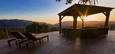 a gazebo with two chairs and the sunset in the mountains at Mountain View Playhouse Near Yosemite & Bass Lake in Oakhurst
