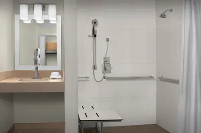 a bathroom with a shower with a bench and a sink at TownePlace Suites Sacramento Cal Expo in Sacramento