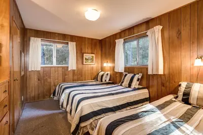 two beds in a room with wooden walls and windows at 2B Quail Meadow in Wawona