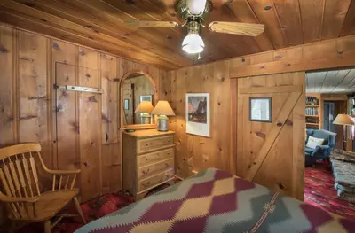 a bedroom with wooden walls and a bed and a ceiling fan at 14 Chipmunk Hollow in Wawona