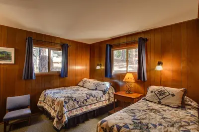 a bedroom with two beds and a chair and two windows at 11B Sequoia House in Wawona