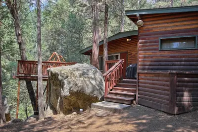 a log cabin with a staircase and a large rock at 1L The Tree House in North Wawona