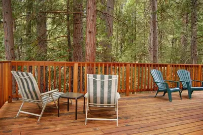 three chairs and a table on a deck with trees at 92 Harmony Villa in Wawona