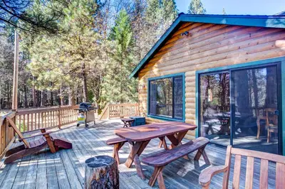 a cabin with a wooden deck with a picnic table and benches at 21 River Refuge in North Wawona