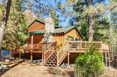 a log cabin in the woods with a large deck at 21 River Refuge in North Wawona