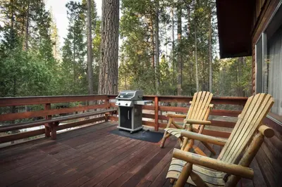 two chairs and a grill on a deck with trees at 23 Arnetts Cabin in North Wawona