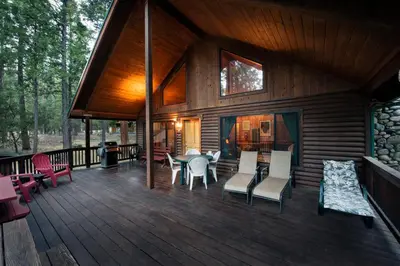 a house with a deck with a table and chairs at 24 Wawona Cabin in Wawona