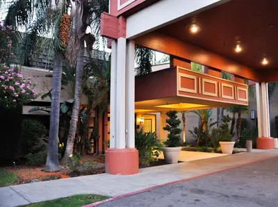a building with a porch with palm trees and plants at Piccadilly Inn Airport in Fresno
