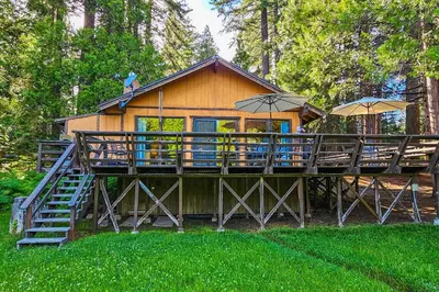 a house with a deck with tables and umbrellas at Water's Edge Retreat in Shaver Lake