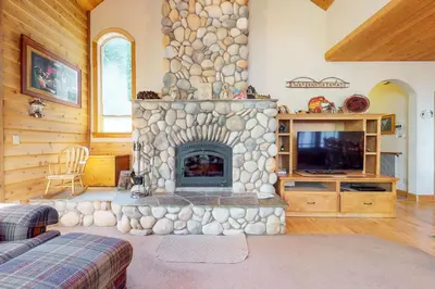 a living room with a stone fireplace and a tv at New England Cottage in Shaver Lake