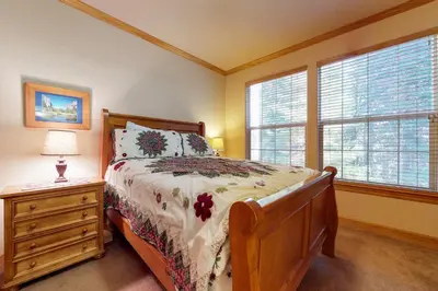 a bedroom with a bed and a nightstand and windows at New England Cottage in Shaver Lake