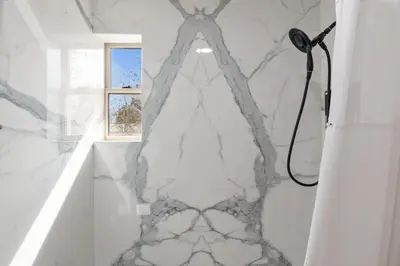 a white marble bathroom with a shower and a window at Lions Gate Hotel in Sacramento