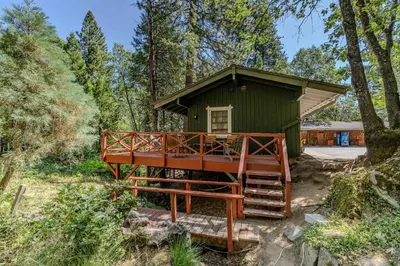 a green cabin in the woods with a large deck at Narrow Gauge Inn in Fish Camp