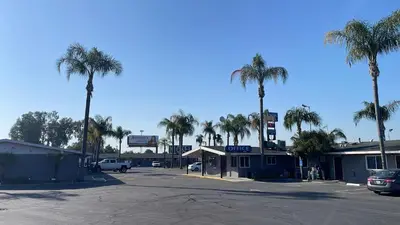 a parking lot with palm trees and a gas station at King's Inn Motel in Kingsburg