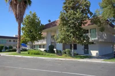 a white building with a balcony and palm trees at Motel 6-Porterville, CA in Porterville