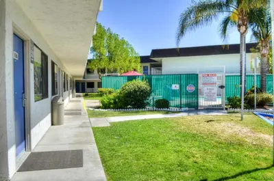 a building with a fence and a grass yard at Motel 6 - Santa Nella, on i-5 in Santa Nella Village