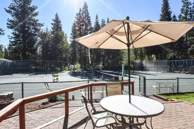 a table and chair with an umbrella on a tennis court at Ski Trails 4113 in Truckee