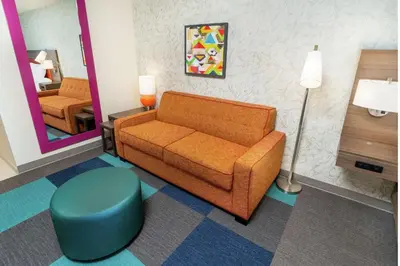 a living room with a couch and a stool and a mirror at Home2 Suites By Hilton Roseville Sacramento in Roseville