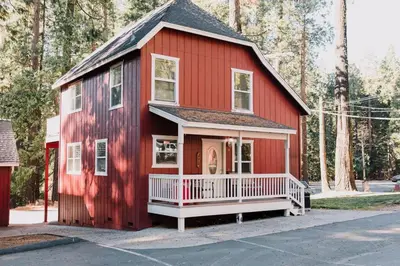 a red house with a white porch in front of trees at The Long Barn Lodge in Long Barn