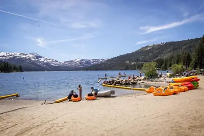 a group of people sitting on a beach next to a lake at Lake Front Family Home at Donner in Truckee