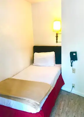 a small bed in a room with a light on the wall at El Dorado Motel in Twain Harte