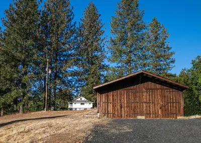 a wooden barn on a hill with a house in the background at Inn at Sugar Pine Ranch in Groveland
