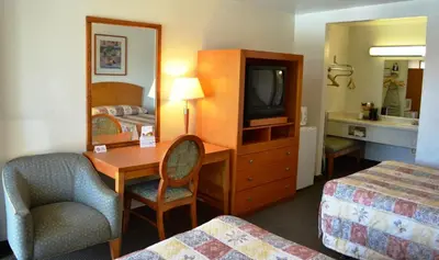 a hotel room with a bedroom with a desk and a tv at Fresno Inn in Fresno