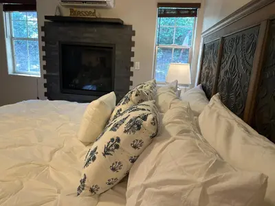a white bed with pillows on it with a fireplace at YoBee! Park Reservation Included! Heart of Yosemite - Homey Studios and Breakfast in Yosemite West